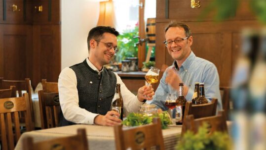 Foto von Michael und Christian Sperber, die mit Sperber-Bräu eine eigene Brauerei betreiben. Sie betrachten Bier in einem Bierglas und wissen, dass Bier ein großer Genuss ist dank vieler Aromen.