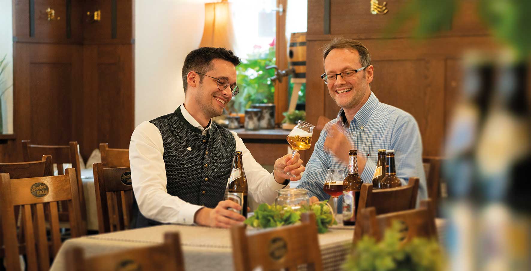 Foto von Michael und Christian Sperber, die mit Sperber-Bräu eine eigene Brauerei betreiben. Sie betrachten Bier in einem Bierglas und wissen, dass Bier ein großer Genuss ist dank vieler Aromen.