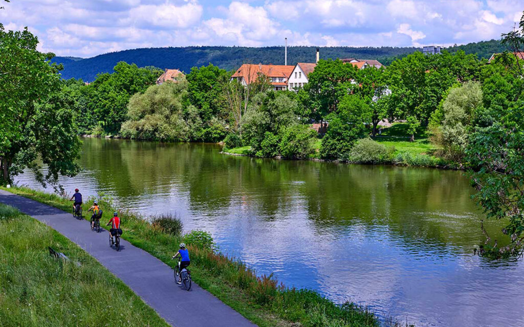 Foto von Radfahrern, die auf dem Radweg Liebliches Taubertal in Baden-Württemberg an einem Fluss entlang fahren
