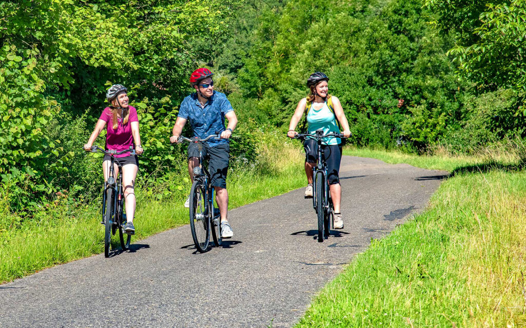 Foto von drei Radfahrern, die auf dem Radweg Liebliches Taubertal etwas entdeckt haben und während der Fahrt nach links schauen.