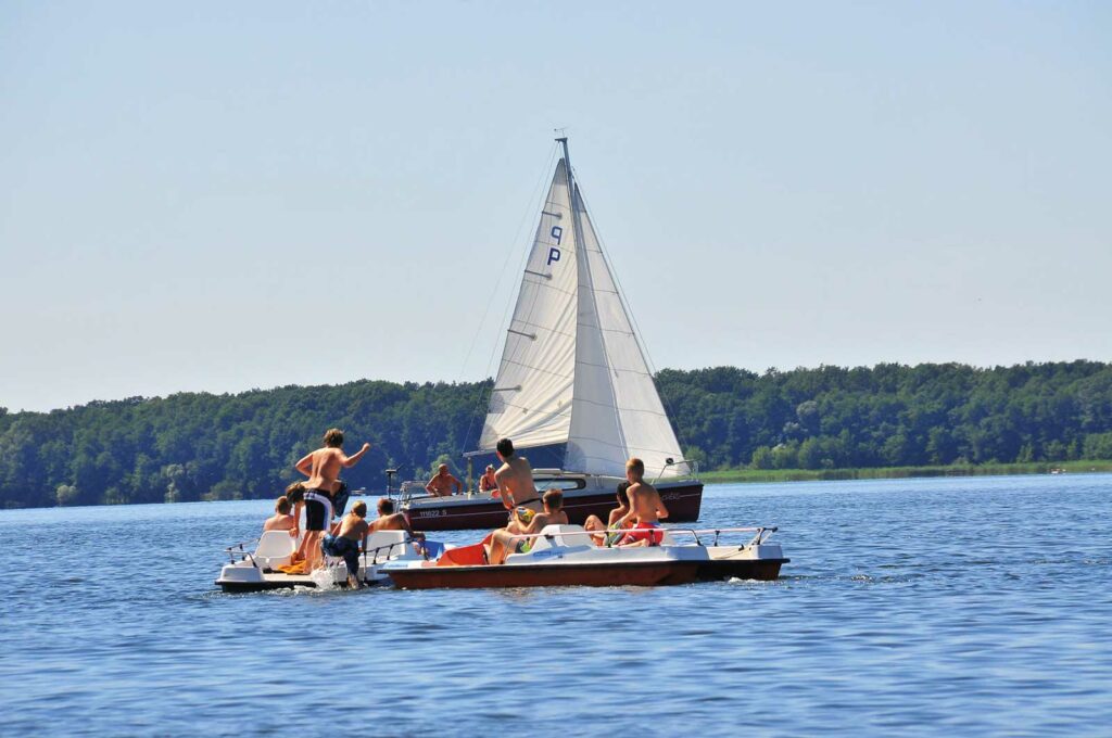 Foto von einem Segelboot und zwei Tretbooten auf dem Arendsee. Die Bootsfahrer genießen ihren Urlaub.