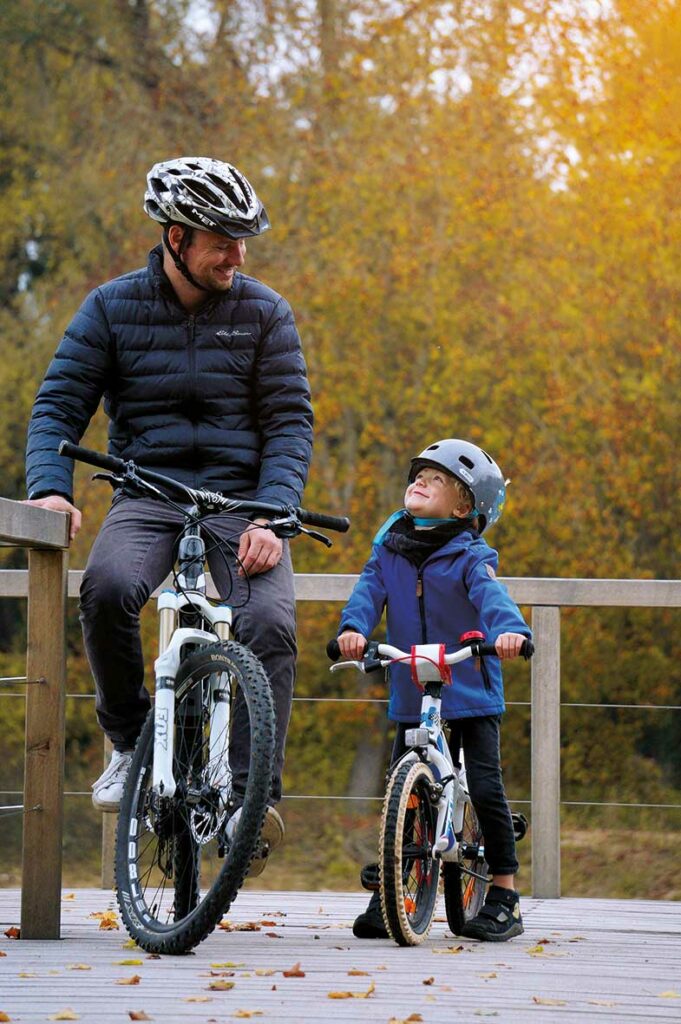 Foto von Vater und Sohn mit Fahrrädern auf dem Holzsteg am Donauursprung in Donaueschingen